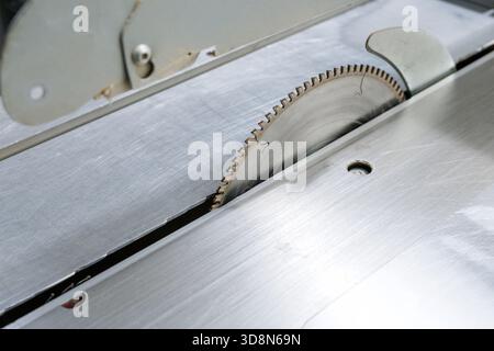 Sharp circular blade of a table saw emerging from metal surface in carpentry workshop concept of industrial safety risk Stock Photo