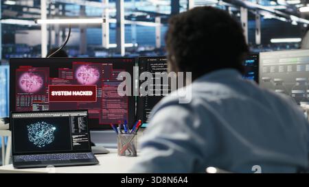 Man with paraplegia in server hub trying to protect hardware from hacker attack stealing sensitive information. Data center specialist in wheelchair fighting virus during security breach, camera B Stock Photo