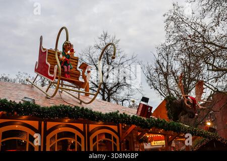 Kiel, Germany - 01. December 2025: Christmas market stall featuring an elf rocking on a sleigh and a moose head wearing a Santa hat, attracting visito Stock Photo