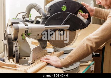 Man using electric miter saw to cut timber trim in carpentry workshop concept of diy home improvement and power tool safety Stock Photo