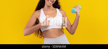 Smiling Woman Exercising With a Dumbbell Against a Bright Yellow Background Stock Photo