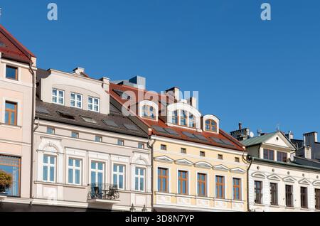 Colorful historic townhouses with ornate windows, detailed facades, and varied roofs stand in a bright urban street under a clear blue sky. Stock Photo