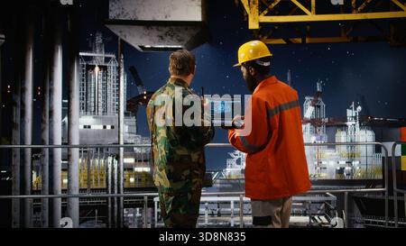 Offshore engineer and naval officer using AI technology on laptop to inspect drilling operations, working with the coastal command post to ensure safe oil extraction activity. Stock Photo