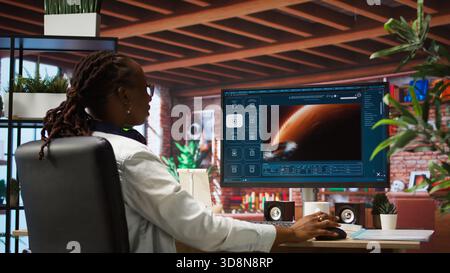 Woman at home using generative artificial intelligence website generating videos using diffusion models. Person drinking coffee and using AI virtual assistant producing clips, camera A Stock Photo