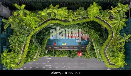 Aerial view of lush greenery cascades over the hotel's terraced balconies and pool, contrasting with the grey city street below, Singapore, Central Si Stock Photo
