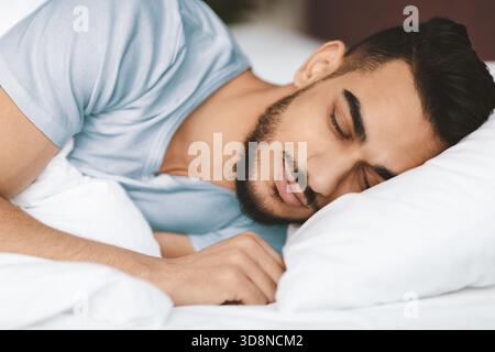 Young Man Resting Peacefully on a Bed in a Cozy Room During Daytime Stock Photo