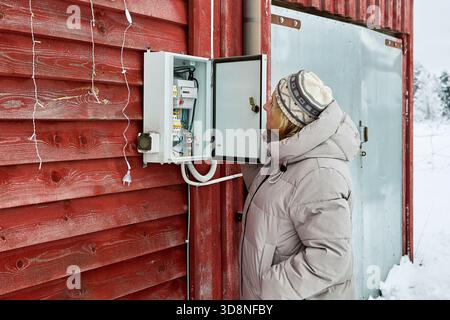 Observing exterior electrical panel homeowner studies breakers and meter installed by utility staff on wall of country house. Stock Photo