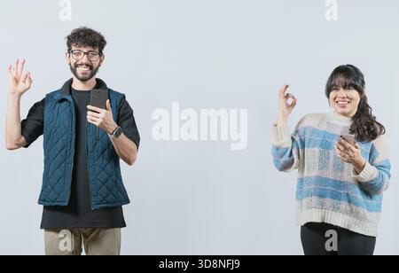 Smiling couple holding a cell phone and gesturing OK, isolated. Happy young couple holding phone gesturing OK Stock Photo