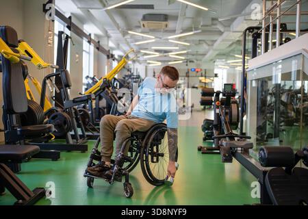 Disabled man in wheelchair at sports center using dumbbell to build upper body and arms strength. Stock Photo
