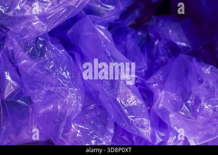 Mysterious purple light glow on crinkled plastic bag pile. An abstract background texture of translucent packaging with dark, clandestine and futurist Stock Photo