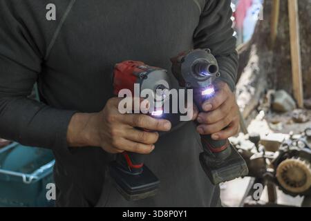 Focused man holding two cordless impact drivers with lights on in workshop. worker compares power tools, showing features of equipment for home improv Stock Photo