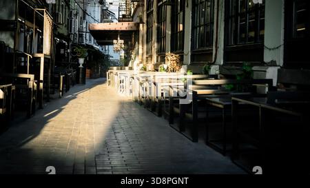 Close-up view of outdoor cafe tables in a quiet alley in Tbilisi, Georgia, bathed in soft morning light and shadows, showcasing the calm elegance of e Stock Photo