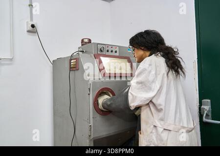 Female worker using a sandblaster machine in a lab setting, focused on a technical process. Industrial expertise Stock Photo
