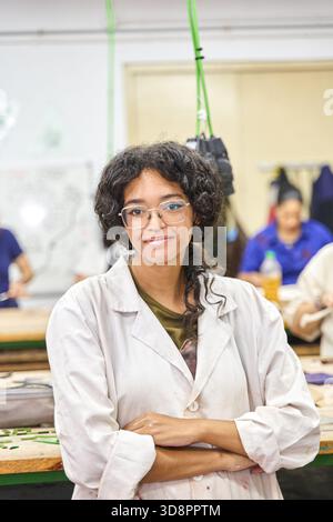Confident black woman student in lab coat and glasses smiling in an art workshop, hands on learning and creative focus, daytime portrait Stock Photo