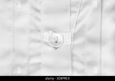 Small white shirt button sewn on white cotton fabric closeup as a background Stock Photo
