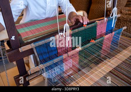 Doha, Qatar - December 01, 2025: Traditional hand-weaving in progress, showing a close-up view of colorful threads arranged on a wooden loom. A crafts Stock Photo