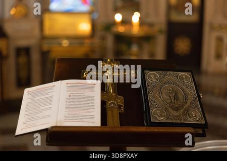 Close-up view of golden Crucifix on stand with open prayer book and ornate Bible in Orthodox church interior during traditional service. Spirituality, Stock Photo