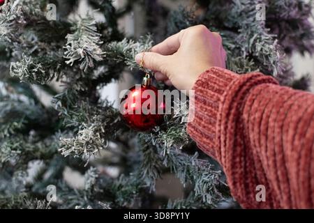 Close-up of a woman’s hand placing a Christmas ornament on a decorated tree Stock Photo