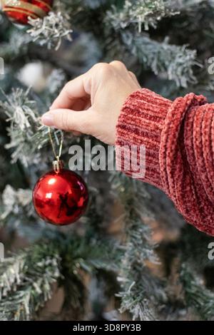 Close-up of a woman’s hand placing a Christmas ornament on a decorated tree Stock Photo
