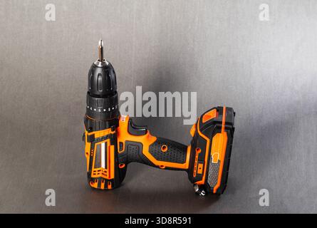 Orange and black cordless electric power drill with a Phillips head screwdriver bit inserted. Tool rests on a seamless gray studio background. Essenti Stock Photo