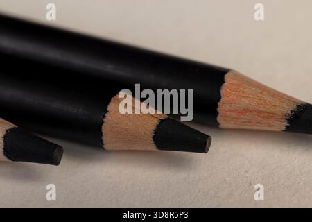 a row of black wooden pencils folded on cheap loose paper, wooden pencils with graphite lead for drawing or other work, close up Stock Photo