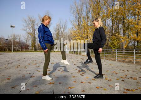 Two middle-aged women doing warm-up exercises in the park on an autumn morning Stock Photo