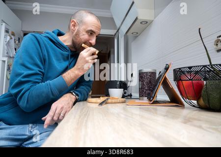 Man having toast for breakfast while using a tablet at home Stock Photo