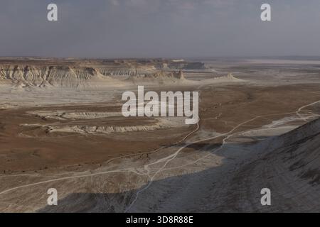 Remote desert Ustyurt plateau featuring white rock formations, eroding cliffs, and winding dirt roads stretching through a vast, untouched geological Stock Photo