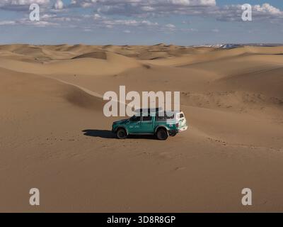 Tough pickup truck powering across sandy desert dunes, off-road adventure under clear blue sky, capturing solitude, vastness and rugged freedom in ari Stock Photo