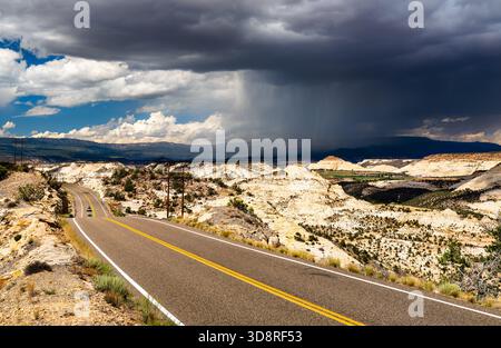 Utah State Route 12 winds over The Hogback in Grand Staircase-Escalante National Monument, United States. A large, dramatic storm cloud with rain, virga, hangs over the vast slickrock landscape Stock Photo