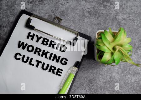 Concept of hybrid working culture write on clipboard isolated on Wooden Table. Stock Photo