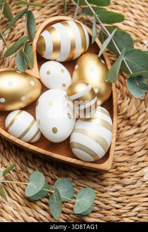 Easter decor. Easter eggs painted in gold in a heart-shaped wooden bowl. The concept of preparation for the celebration. Stock Photo