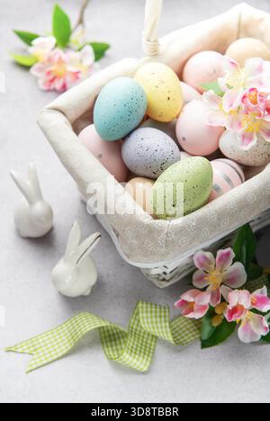 Colorful easter eggs and spring flowers overflowing from a white wicker basket on a light background Stock Photo