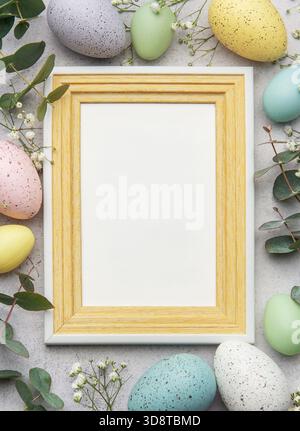 Easter mockup with wooden frame decorated with colorful eggs, eucalyptus leaves and gypsophila flowers on gray concrete background Stock Photo