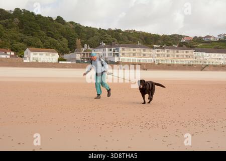 A man walking his dog on the beach at St Brelade's Bay, St Brelade, Jersey, The Channel Islands Stock Photo