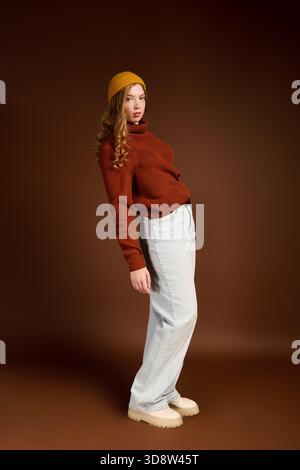 Young woman with lovely red hair poses in a cozy winter sweater against a warm brown background. Stock Photo