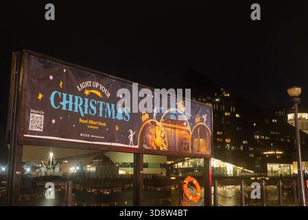 Night scene with illuminated banner promoting Christmas events at Liverpool’s Royal Albert Dock, set against modern waterfront buildings. Stock Photo