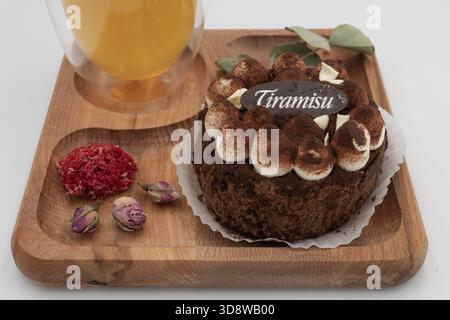 Tiramisu dessert with herbal tea on wooden tray with dried flowers and eucalyptus leaves on a clean white background Stock Photo