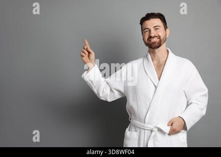 Man in bathrobe pointing at something on grey background. Space for text Stock Photo