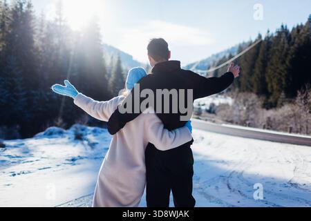 Back view of happy couple in love hugging on background of winter Carpathian mountains by car. Travelling by auto Stock Photo