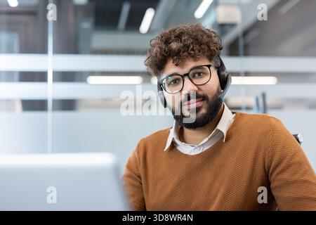 Bearded man with headset at call center desk providing friendly customer and technical support, working professionally in an office helping clients via phone and online communication Stock Photo