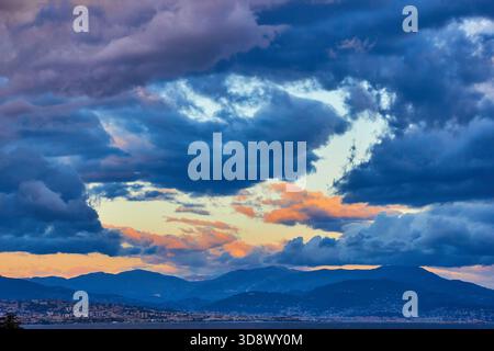 Dramatic Sunset Over Cloudy Sky, Mountain Range, And City Skyline Stock Photo
