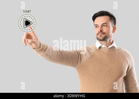 Young businesswoman pressing start button on virtual screen against grey background Stock Photo