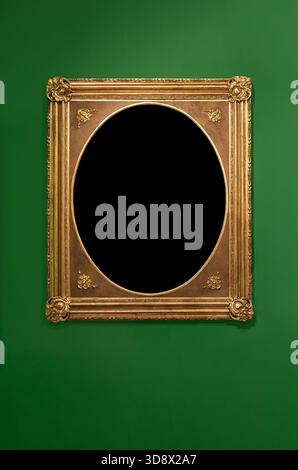 Ornate golden rectangular frame with an oval opening hanging on a solid green wall. Stock Photo