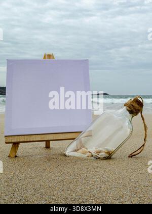 Vertical close up of a blank canvas on an easel and a bottle with shells on the sand. Waves and cloudy sky in the background. Ideal for copy space or Stock Photo