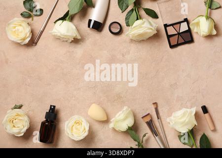 Frame made of white rose flowers, bottle of cosmetic product and makeup products on beige grunge background Stock Photo