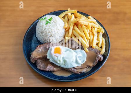 Delicious bitoque de vaca served with fried potatoes and rice, featuring a perfectly cooked egg on top, showcasing a traditional meal presentation Stock Photo