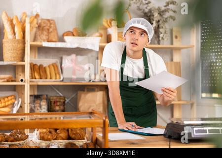 Thoughtful young baker looking over papers in craft bakery Stock Photo