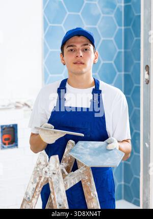 Construction worker in work clothes engaged in wall tiling work during overhauls indoors Stock Photo