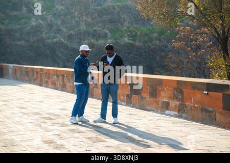 Yerevan Armenia 10.25.2025. Two men are standing on a bridge, one of them is looking at his cell phone. Scene is casual and relaxed, as the two men ar Stock Photo